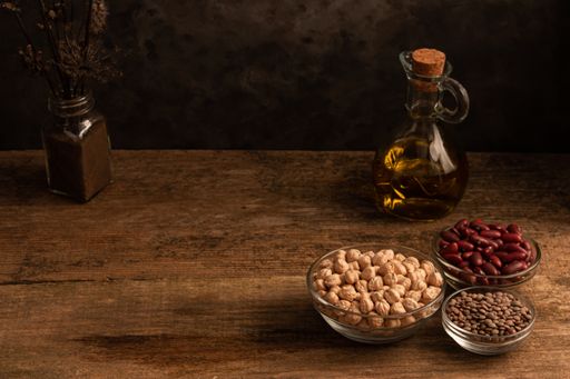 A low angle shot of oil and three bowls of chickpea, red beans, lentil on a wooden table