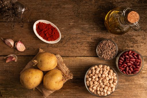 A top view of potatoes, 3 bowls of chickpea, red beans and lentil and other ingredients on the table