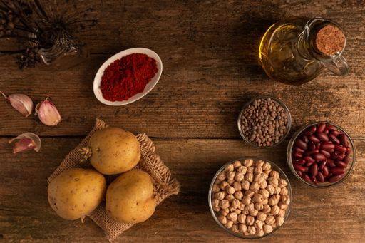 A top view of potatoes, 3 bowls of chickpea, red beans and lentil and other ingredients on the table