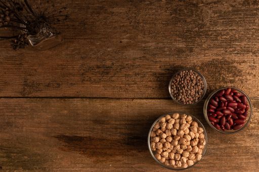 A top view shot of three bowls of chickpea, red beans and lentil on a wooden table