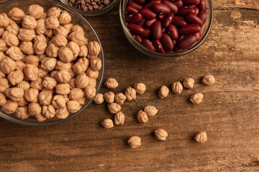A top view shot of three bowls of chickpea, red beans and lentil on a wooden table