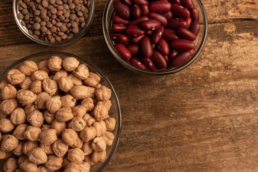 A top view shot of three bowls of chickpea, red beans and lentil on a wooden table