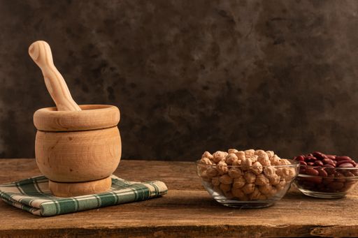 A mortar with pestle made of wood, 3 bowls of chickpea, red beans, lentil on the table