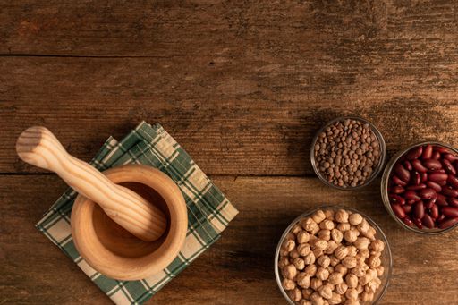 A top view of a mortar with pestle made of wood, 3 bowls of chickpea, red beans, lentil on the table