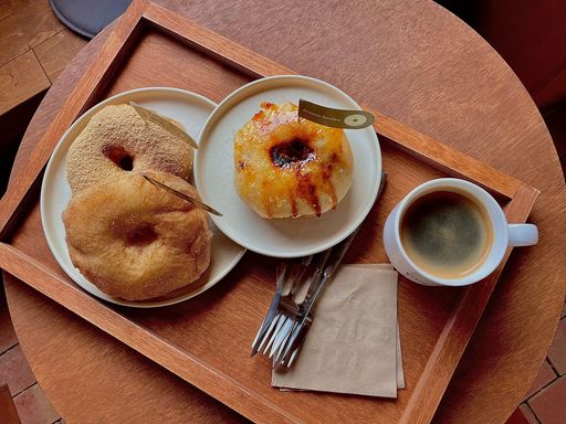 A top view of cup of hot americano and sweet donuts on wooden tray