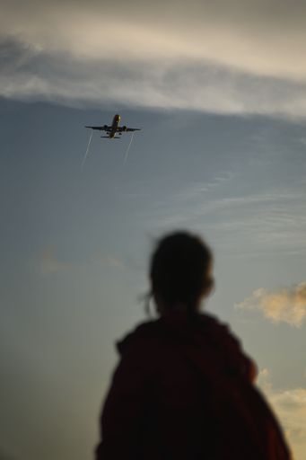 An aerial view of an airplane flying over an airport with a person in the foreground looking up in awe