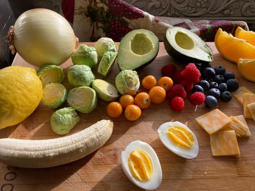 A top view shot of fresh fruits and vegetables and a boiled egg on a wooden cutting board