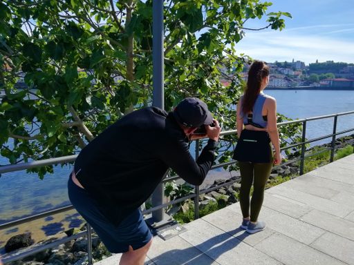 A male photographer taking a photo of a lady's back standing on the bay of a river on a sunny day