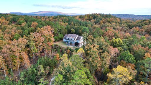 An aerial shot of a building on top of a hill in the middle of a forest during autumn