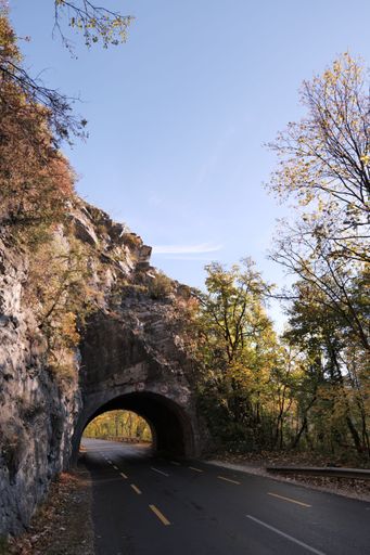 A road passing through the small tunnel in the rocky mountain, surrounded by green nature, on a sunny day