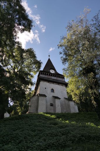 A low-angle shot of a Gothic Protestant Church of Avas, tucked among green trees on a sunny day, with clouds in the sky