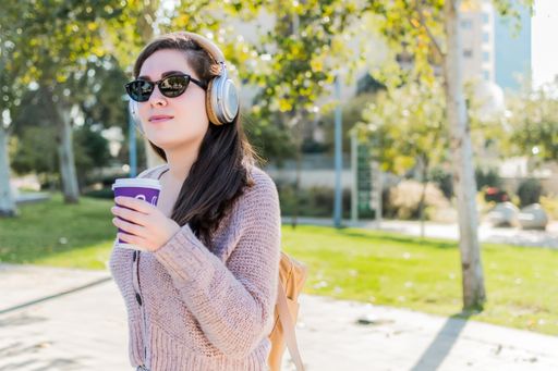 A woman with headphones listening to music and drinking coffee sitting in a park