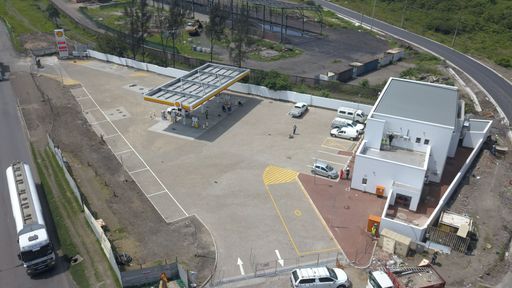A drone view of petrol station and parking lot with bus on the road on a sunny day