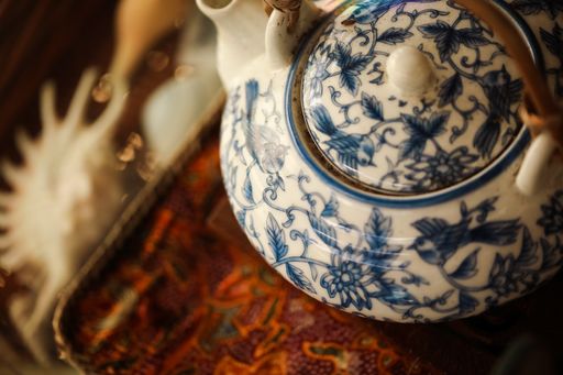A ceramic teapot with blue decorations on a tray under the lights with a blurry background