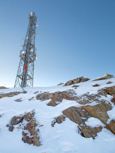 communications tower with mobile phone antennas on top of a snowy mountain, view from below, vertical