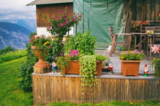 A wooden terrace, decorated with plants in pots and lots of flowers in front of the barn in the mountains with a great view in the valley.