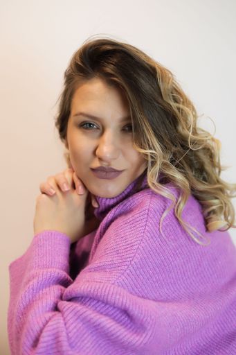 A portrait of a young woman in a stylish purple sweater, happily posing against a white background