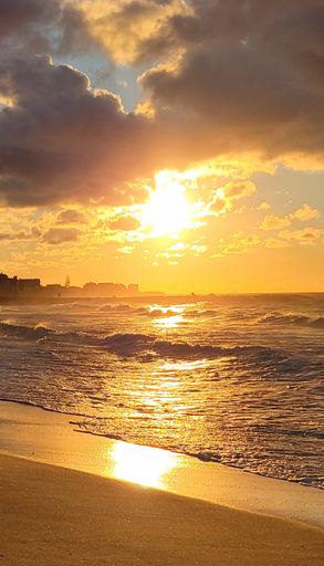 A vertical shot of the sun that is about to set across the sea from a beach