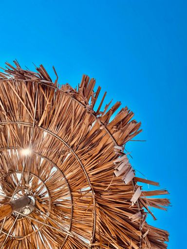 A low angle shot of a straw umbrella against a cloudless blue sky on a sunny day