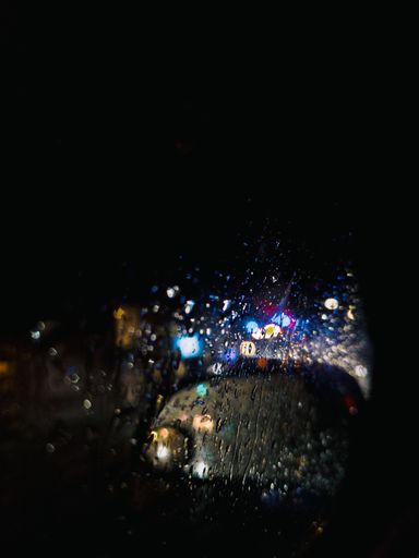 A vertical shot of car side view mirror and window covered with raindrops at night