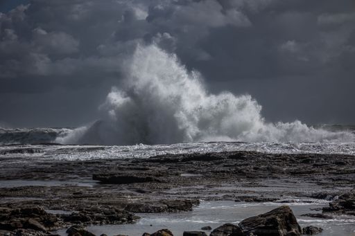 A Wave crashing on shore rocks during stormy weather, dramatic dark sky, and spray flying