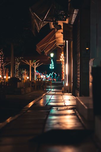 A vertical shot of an empty street with closed stores, colorful city lights