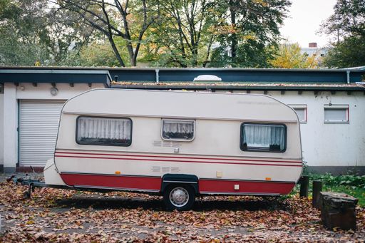 An old Mercedes caravan is parked on the road in autumn. The camper is surrounded by leaves and fallen leaves.