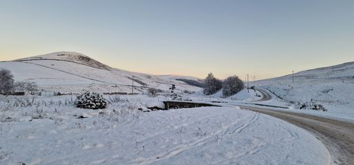 A panoramic view of a mountain range covered with snow during an orange sunset