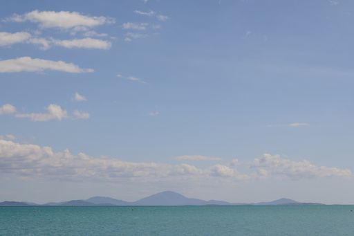 A wide angle shot of the ocean surrounded by mountains under the blue sky