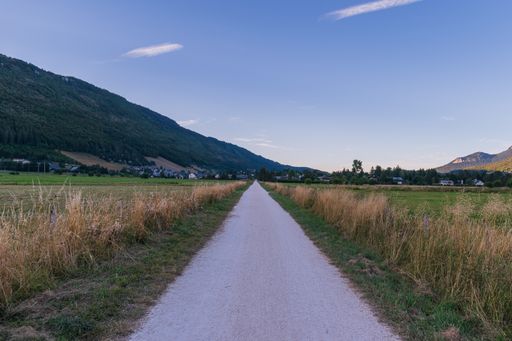 A beautiful view of a narrow road in a grassy field surrounded by rocky mountains
