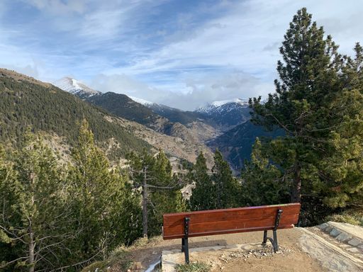 A wooden bench on the edge of a hill with scenic green mounts in front of it