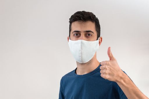 A young man gesturing the like sign while wearing a mask to cover his mouth