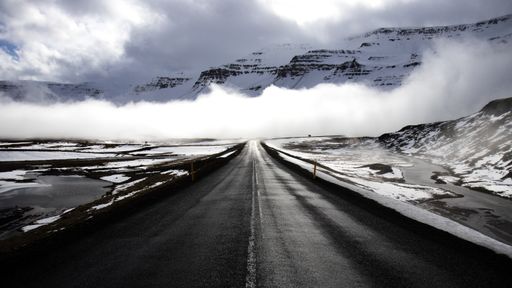 A mesmerizing shot of a long straight road leading towards snow-capped mountains