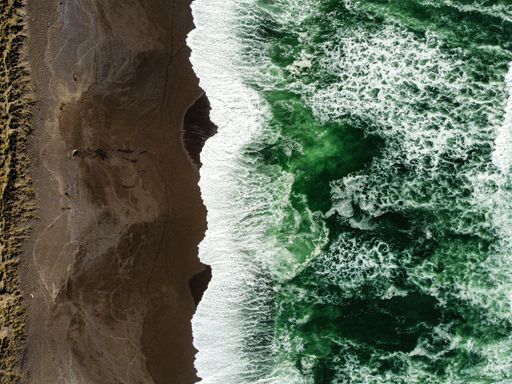 A drone shot of the gorgeous teal waves of the ocean near the sandy shore