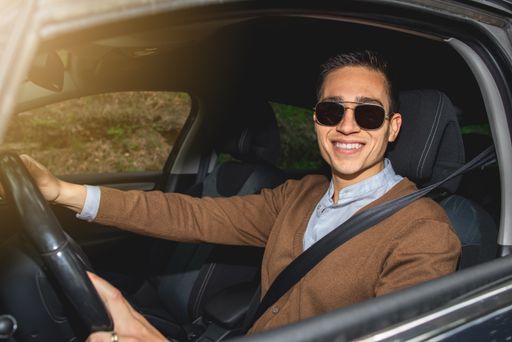 A happy CAucasian man with sunglasses sitting in the car and smiling