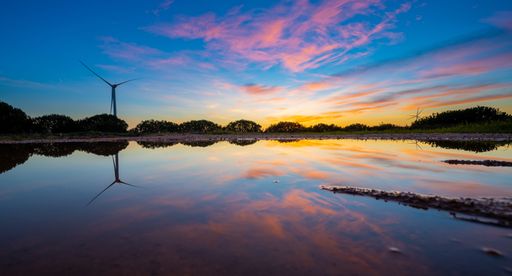 A wide angle of the beautiful nature scene with a lake with the reflection of trees and wind turbine with a beautiful sky at sunset
