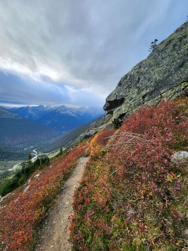 A vertical shot of a narrow path on on the mountainside with the snowy mountains in the background