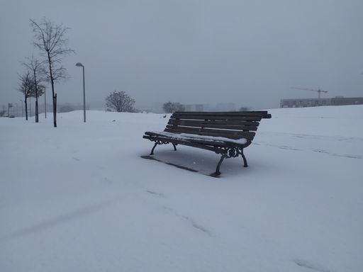 A bench on a field covered in snow on a foggy day