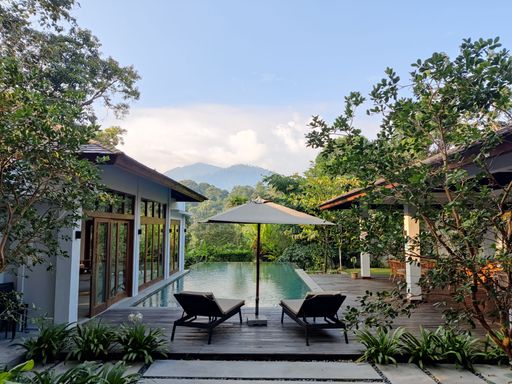A quiet view of two Lounge Chairs by a pool with wooden houses and trees in Janda Baik, Kuala Lumpur