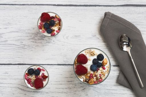 table top shot of natural yogurt with raspberries and blueberries in a glass on a white wooden background, clean and airy look
