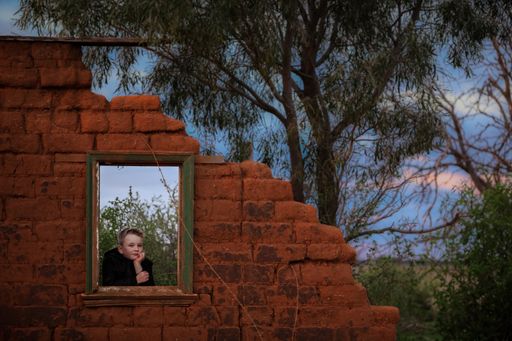 A beautiful view of a little blond boy in a ruined old building looking from the broken window