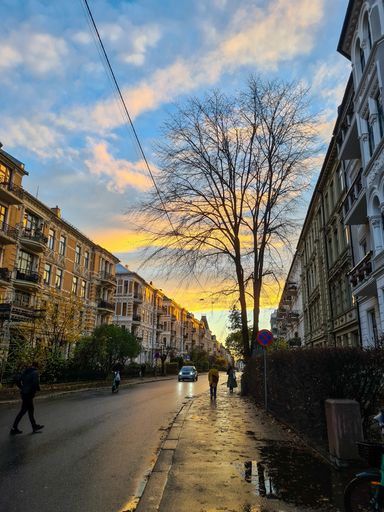 A beautiful view of people walking down the street, at sunset, after the rain, with a car passing by