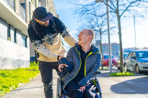 A companion cheerfully talking with a young man in a wheelchair on the sidewalk