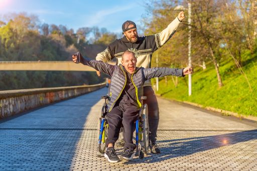 A disabled person in wheelchair with friend overjoyed, smiling, enjoying with arms up