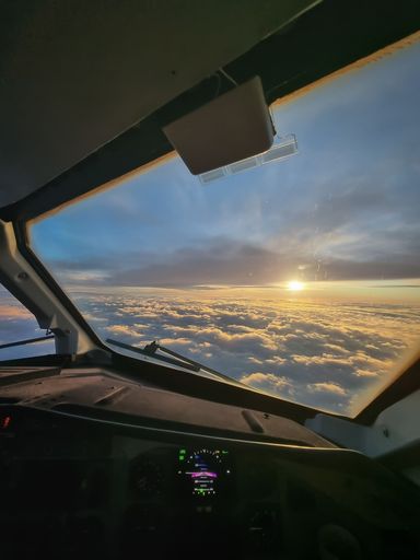 A stunning aerial view of the clouds illuminated by the sunset seen through the window of an airplane
