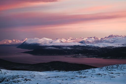 A river and the rocky mountains covered with snow during scenic pink sunset, Tromso, Norway