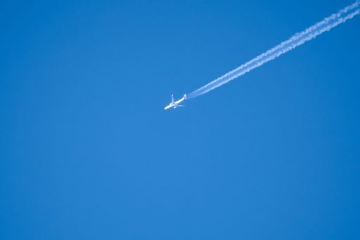 A twin engine jet airliner in deep blue sky with vapor contrails diagonally across the frame.