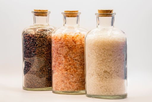 Three glass jars with cork lids containing white, pink, and brown natural salt rock granules