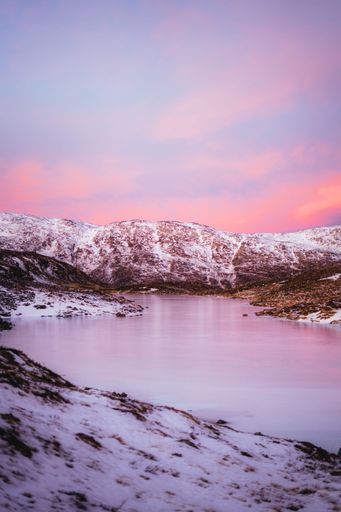 A river and the rocky mountains covered with snow during pink sunset, Tromso, Norway