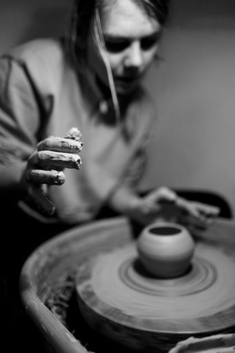 A woman is making a clay bowl on a pottery wheel.
